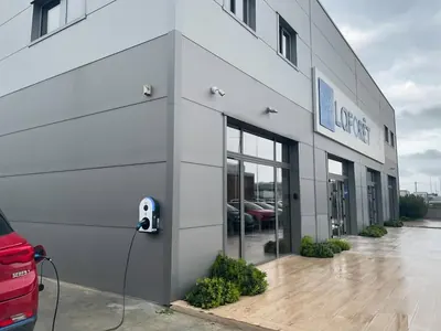 Façade grise de l'agence immobilière Laforêt de Lucciana, avec une borne de recharge murale près de l'entrée et une voiture rouge branchée