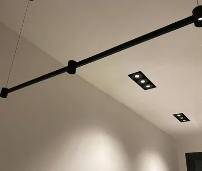 Rail d'éclairage noir au plafond et spots encastrés, dans une pièce aux murs blancs
