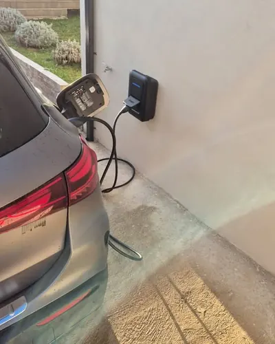 Voiture grise branchée sur une borne murale, le long d'un mur clair